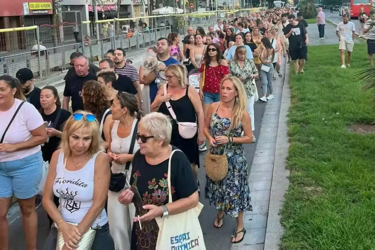 Una multitud de persones camina per una vorera al costat d’un carrer i una zona de gespa en un entorn urbà durant el dia. Una multitud de persones camina per una vorera al costat d’un carrer i una zona de gespa en un entorn urbà durant el dia.