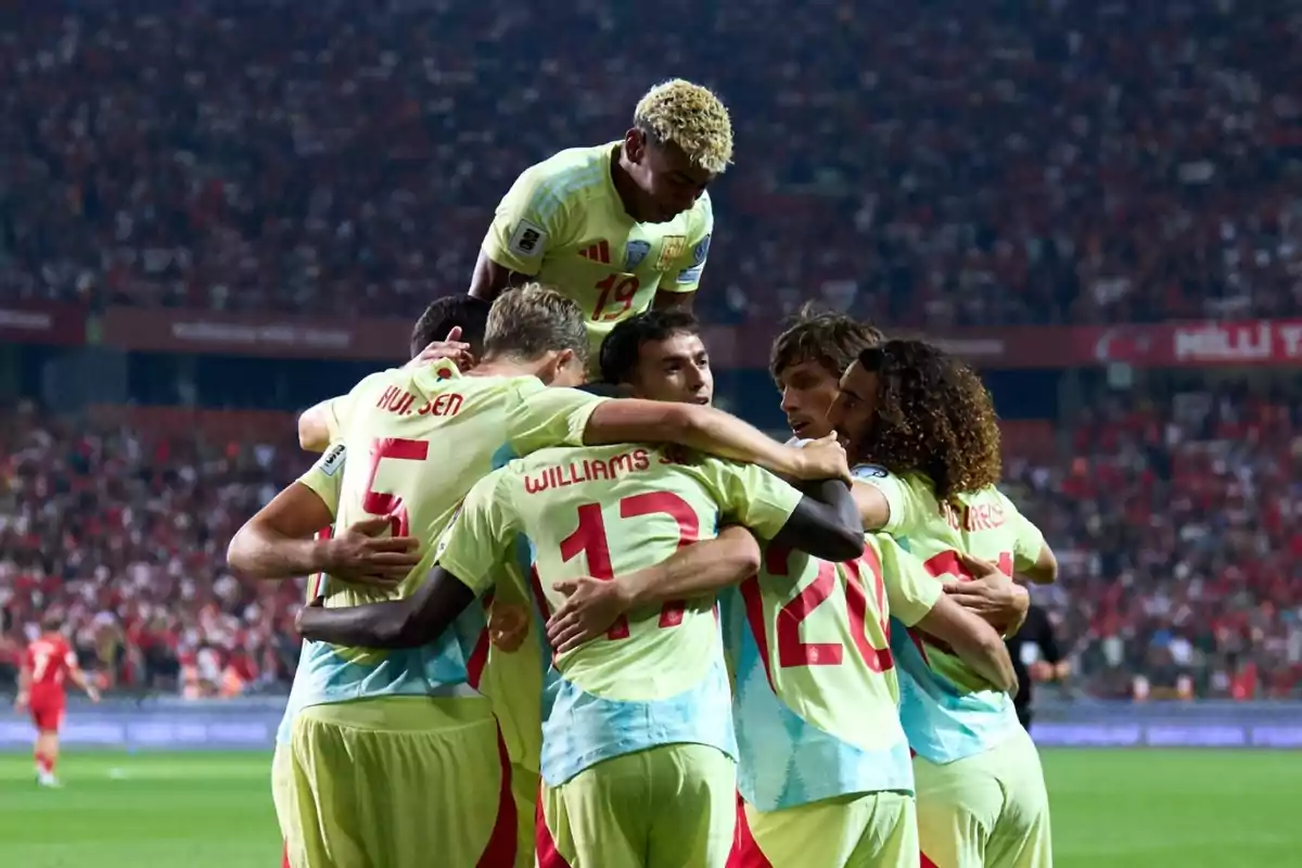Soccer players celebrate a goal by hugging on the field during a match with a stadium full of fans in the background. Soccer players celebrate a goal by hugging on the field during a match with a stadium full of fans in the background.