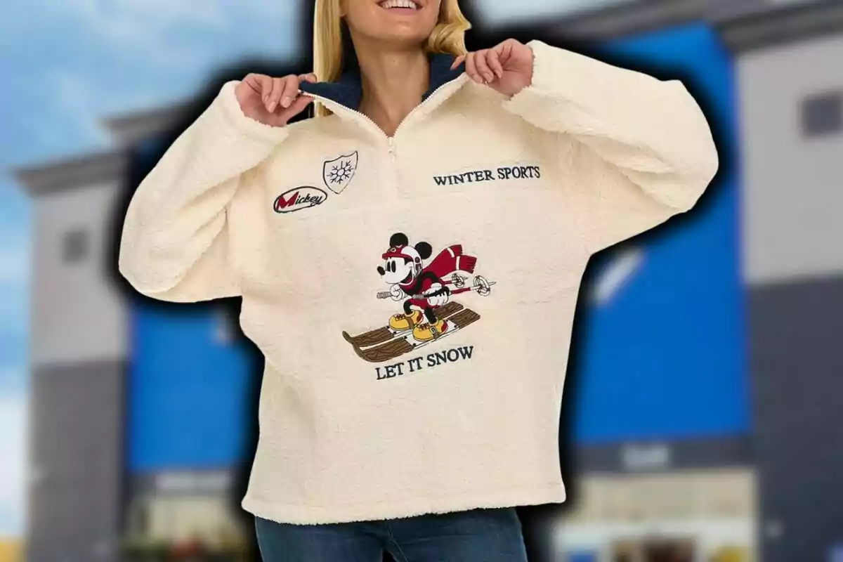 Woman smiling wearing a beige plush sweater with a design of Mickey Mouse skiing and the words Winter Sports and Let it Snow. Woman smiling wearing a beige plush sweater with a design of Mickey Mouse skiing and the words Winter Sports and Let it Snow.