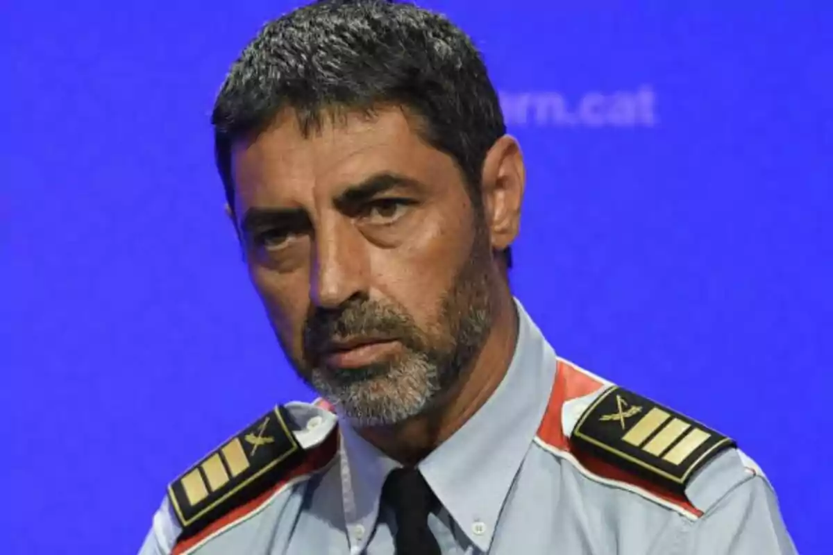 Home amb uniforme de policia i expressió seriosa sobre fons blau