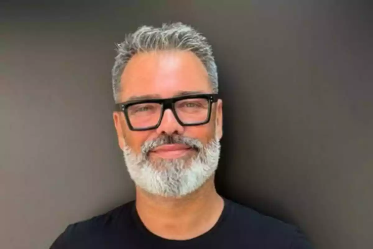 Hombre con barba y gafas, que es el peluquero Víctor del Valle, y camiseta oscura posando frente a un fondo gris.