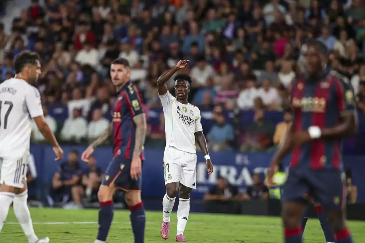 Futbolistes de dos equips diferents al camp durant un partit amb públic a les grades al fons