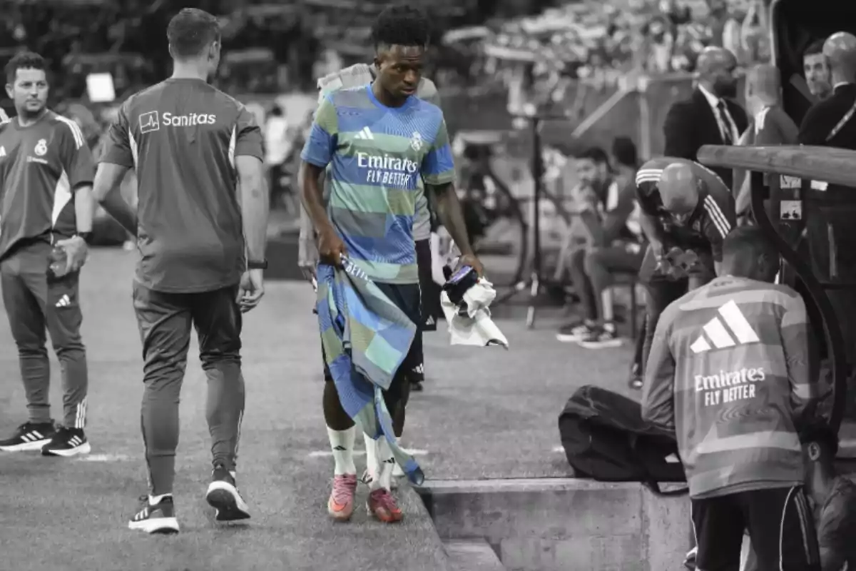 Un futbolista del Reial Madrid amb l’uniforme d’entrenament en color camina cap a la banqueta mentre la resta de la imatge és en blanc i negre.