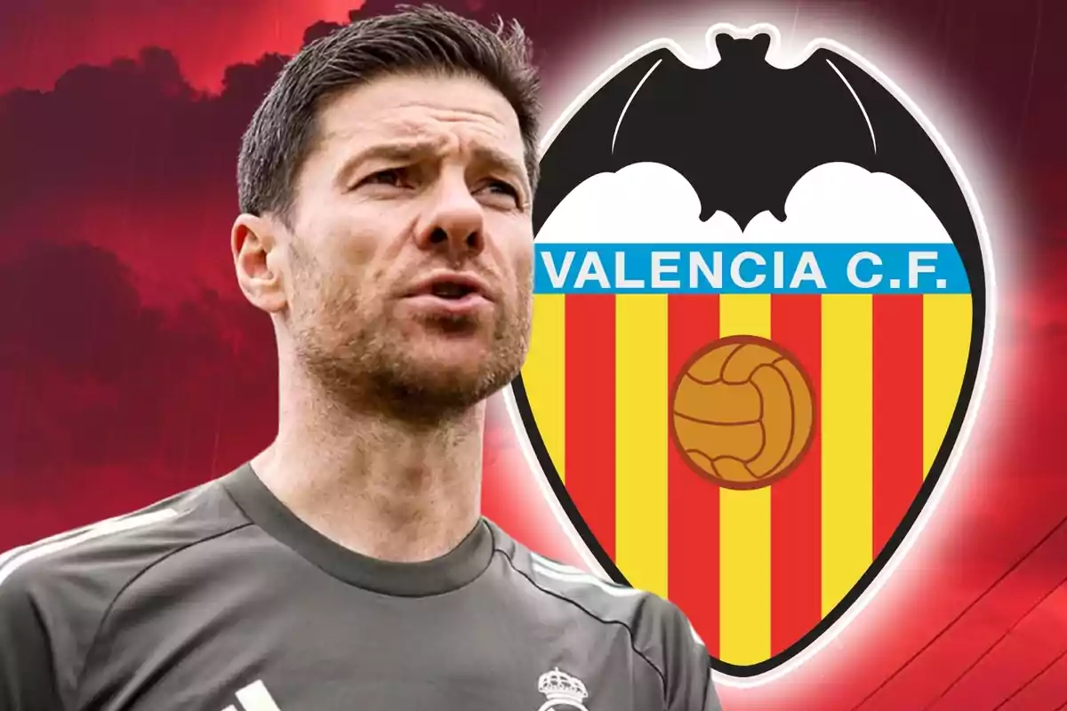 Entrenador de fútbol con camiseta gris al frente del escudo del Valencia CF sobre un fondo rojo