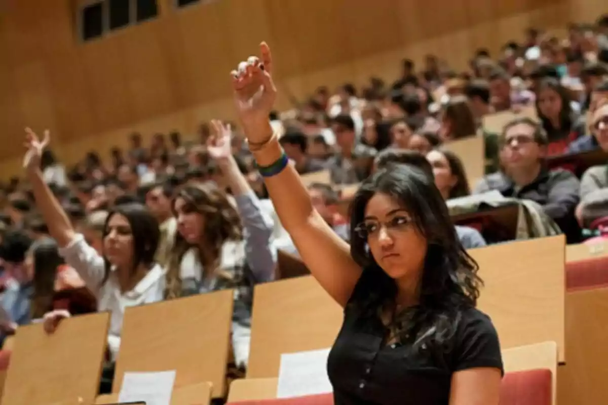 Estudiantes en un auditorio universitario levantando la mano para participar