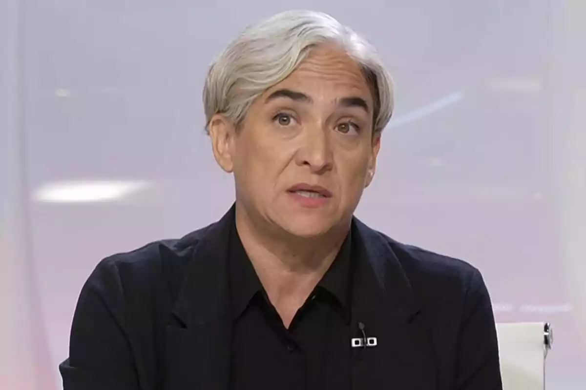 Persona de cabello corto y canoso con expresión seria vestida con ropa oscura en un entorno de estudio de televisión Persona de cabello corto y canoso con expresión seria vestida con ropa oscura en un entorno de estudio de televisión