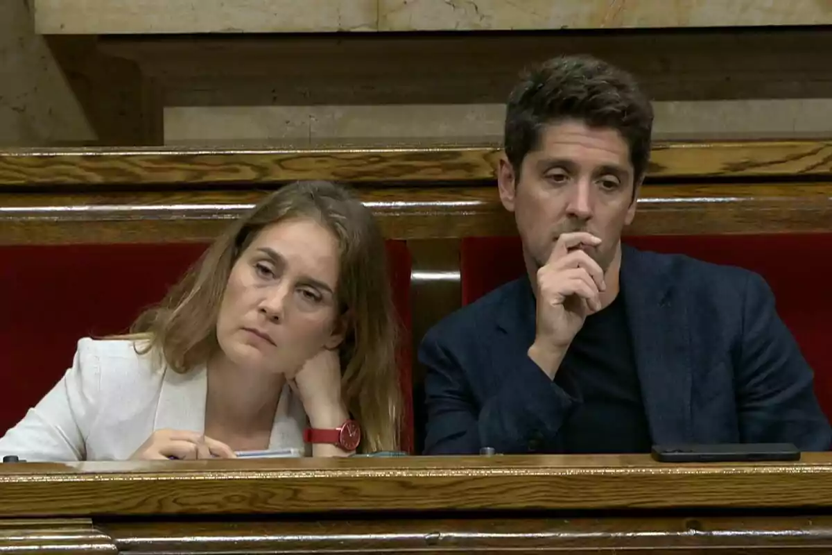 Dos personas sentadas en un banco de madera con expresión seria y pensativa