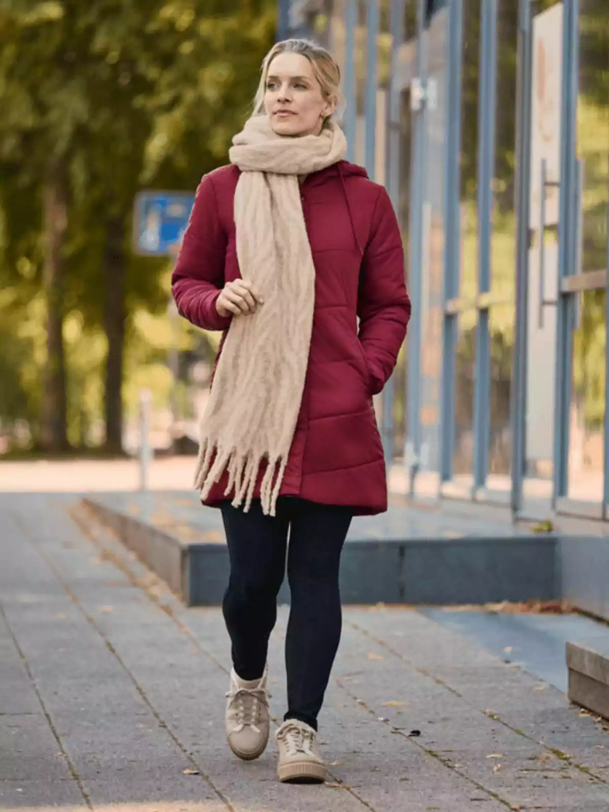 Mujer caminando por la ciudad con abrigo rojo, bufanda beige, leggings negros y tenis claros en un día fresco Mujer caminando por la ciudad con abrigo rojo, bufanda beige, leggings negros y tenis claros en un día fresco