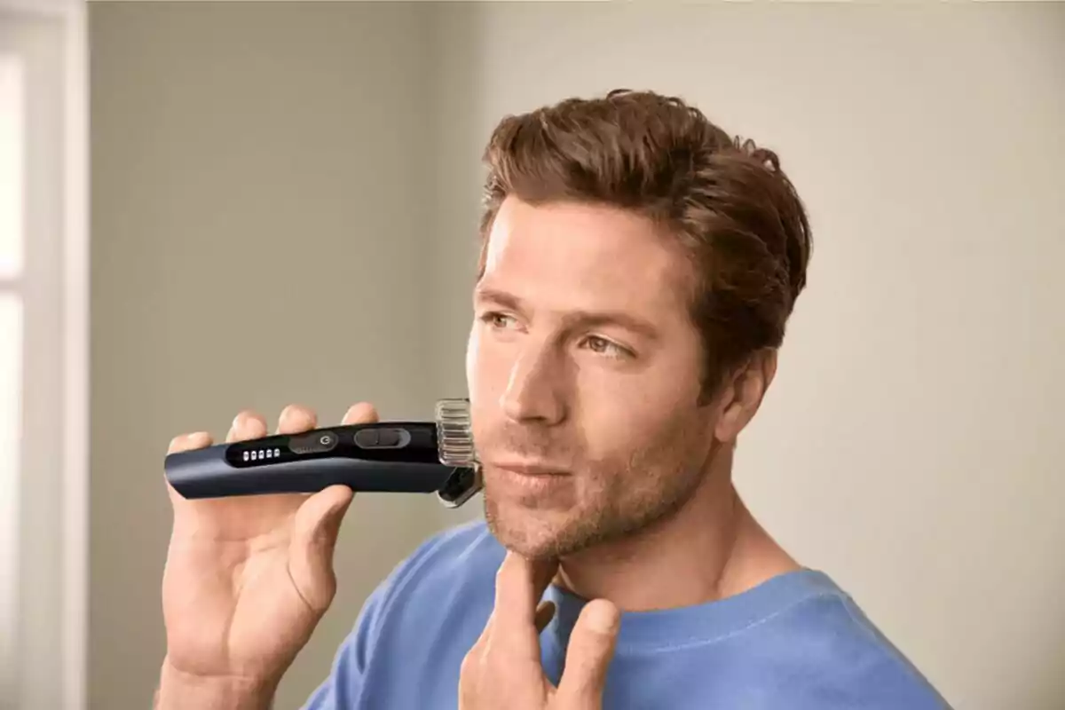 Hombre usando una recortadora eléctrica para arreglar su barba mientras se mira al espejo Hombre usando una recortadora eléctrica para arreglar su barba mientras se mira al espejo