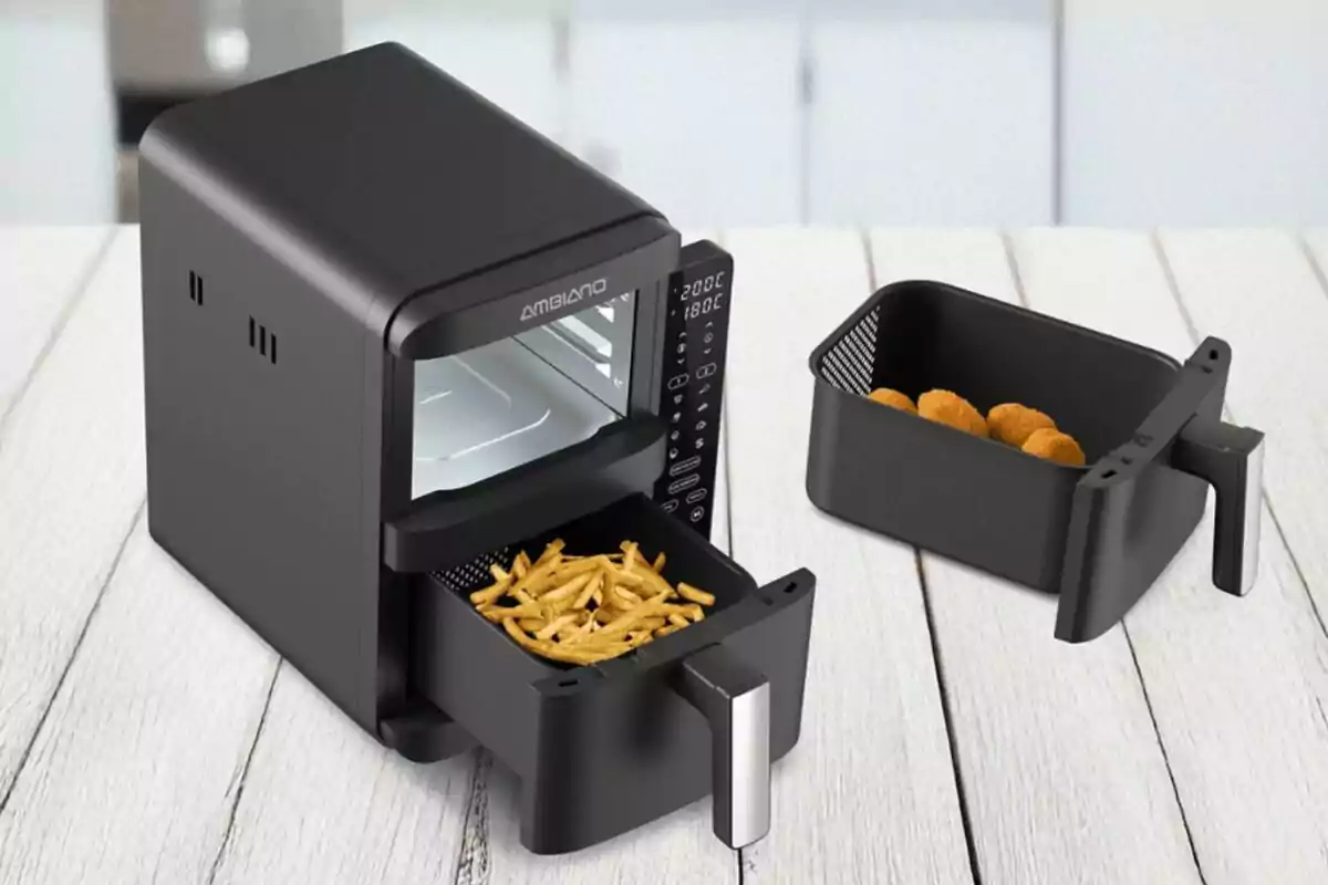 Fregidora d’aire negra amb patates fregides en una safata i una altra safata amb croquetes sobre una taula blanca Fregidora d’aire negra amb patates fregides en una safata i una altra safata amb croquetes sobre una taula blanca