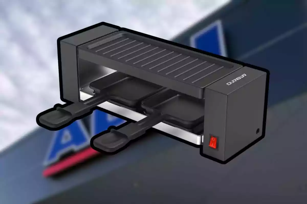 Parrilla eléctrica pequeña de color negro con dos bandejas deslizables y un interruptor rojo, sobre un fondo desenfocado. Parrilla eléctrica pequeña de color negro con dos bandejas deslizables y un interruptor rojo, sobre un fondo desenfocado.