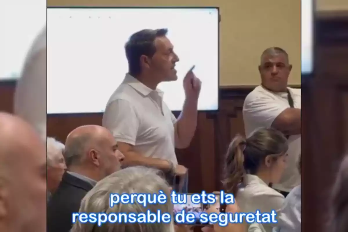 Un hombre de pie habla señalando con el dedo en una sala llena de personas mientras en la parte inferior aparece el texto en catalán "perquè tu ets la responsable de seguretat"