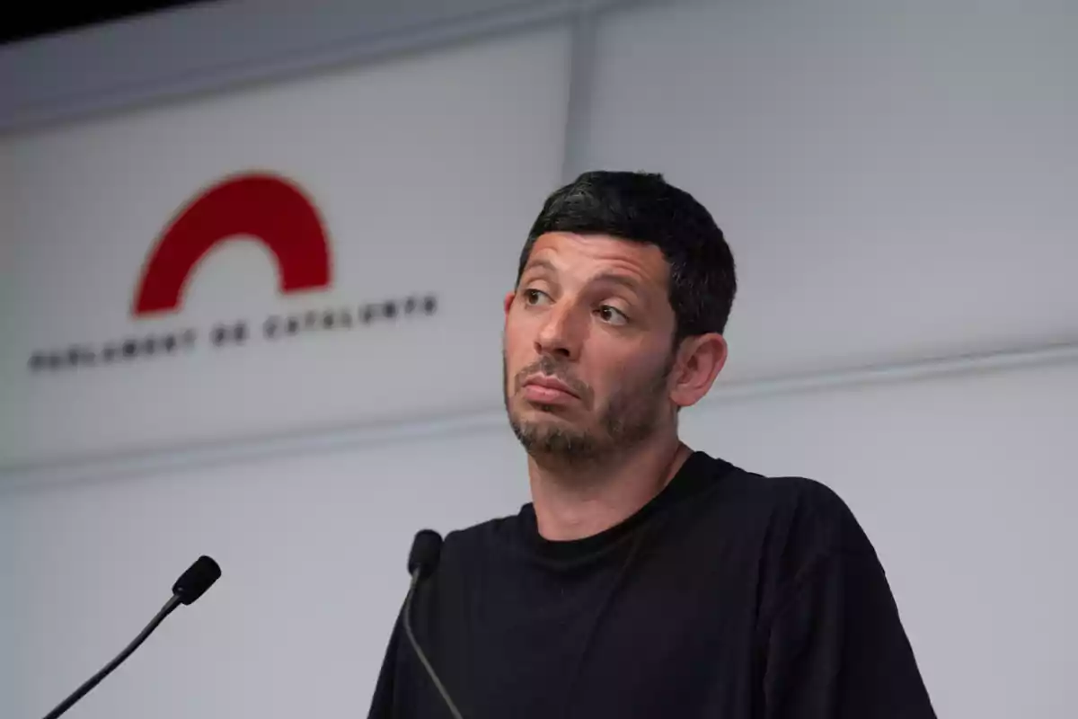 Hombre con camiseta negra hablando en una rueda de prensa en el Parlament de Catalunya