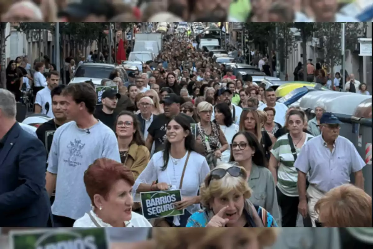 Una multitud de personas camina por una calle durante una manifestación, algunas sostienen carteles que piden barrios seguros.