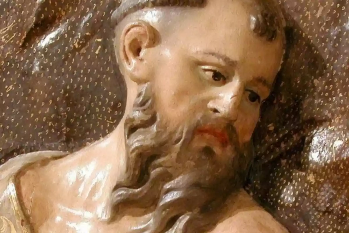 Escultura de un hombre barbudo con expresión seria y fondo decorativo