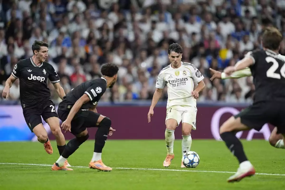 Un jugador del Reial Madrid controla la pilota mentre és envoltat per tres futbolistes de la Juventus durant un partit de futbol en un estadi ple d’espectadors.