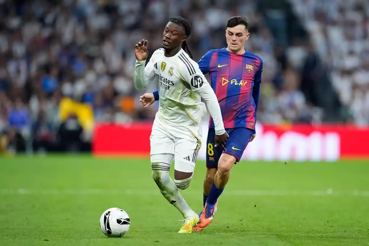Two players from the teams Real Madrid and Barcelona compete for the ball during a match in a stadium full of spectators.