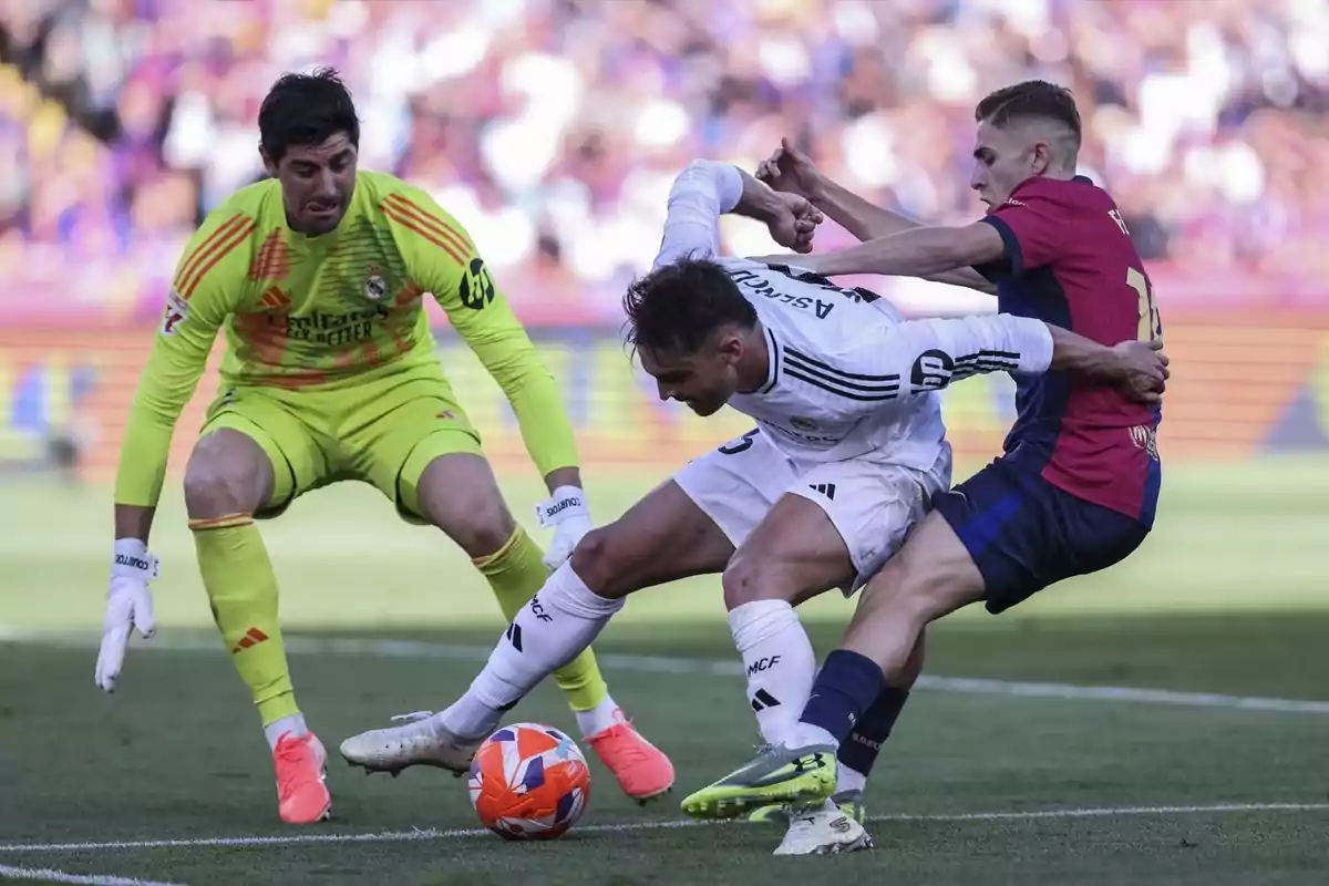 Porter vestit de groc observa mentre dos futbolistes lluiten per la pilota durant un partit de futbol.