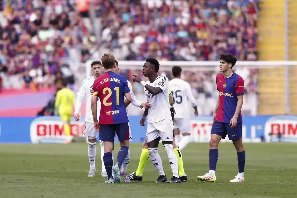 Jugadores de Barcelona y Real Madrid discuten en el campo durante un partido de fútbol con el público de fondo