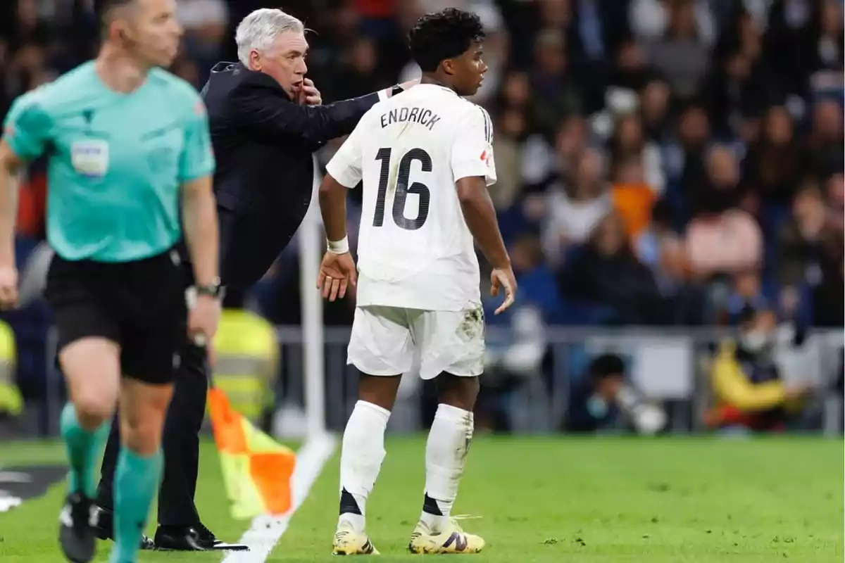 Coach giving instructions to a player wearing the number 16 jersey during a soccer match while a referee walks nearby on the field
