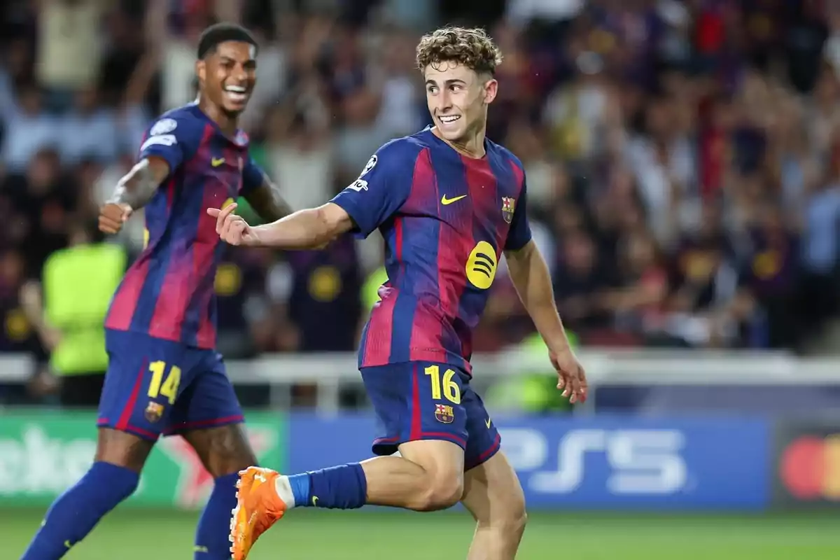 Dos jugadors del Barcelona celebren un gol en un partit de futbol, un d’ells somriu mentre corre i l’altre el segueix amb els braços estesos.