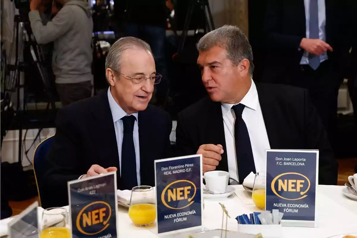 Dos hombres con traje conversan sentados en una mesa redonda durante un evento del Nueva Economía Fórum con jugos de naranja y café sobre la mesa