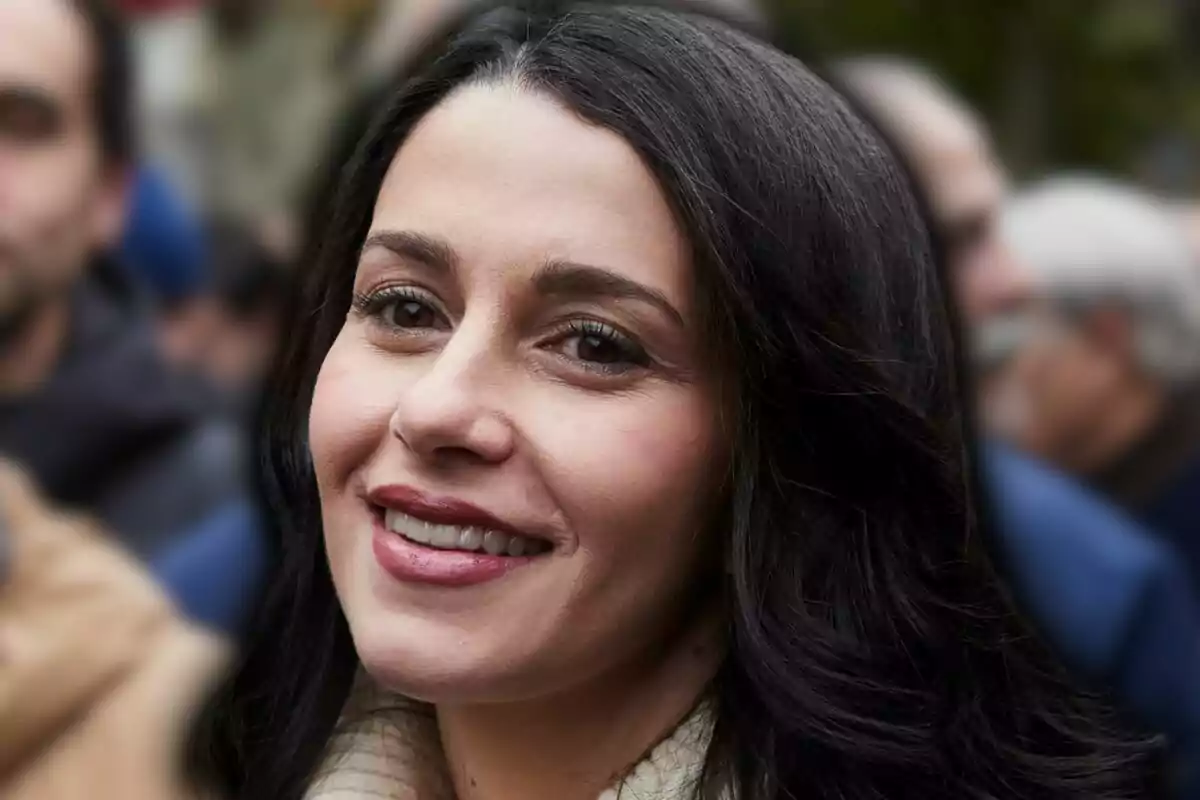 Dona de cabells foscos i llargs somrient a l’aire lliure amb persones desenfocades al fons