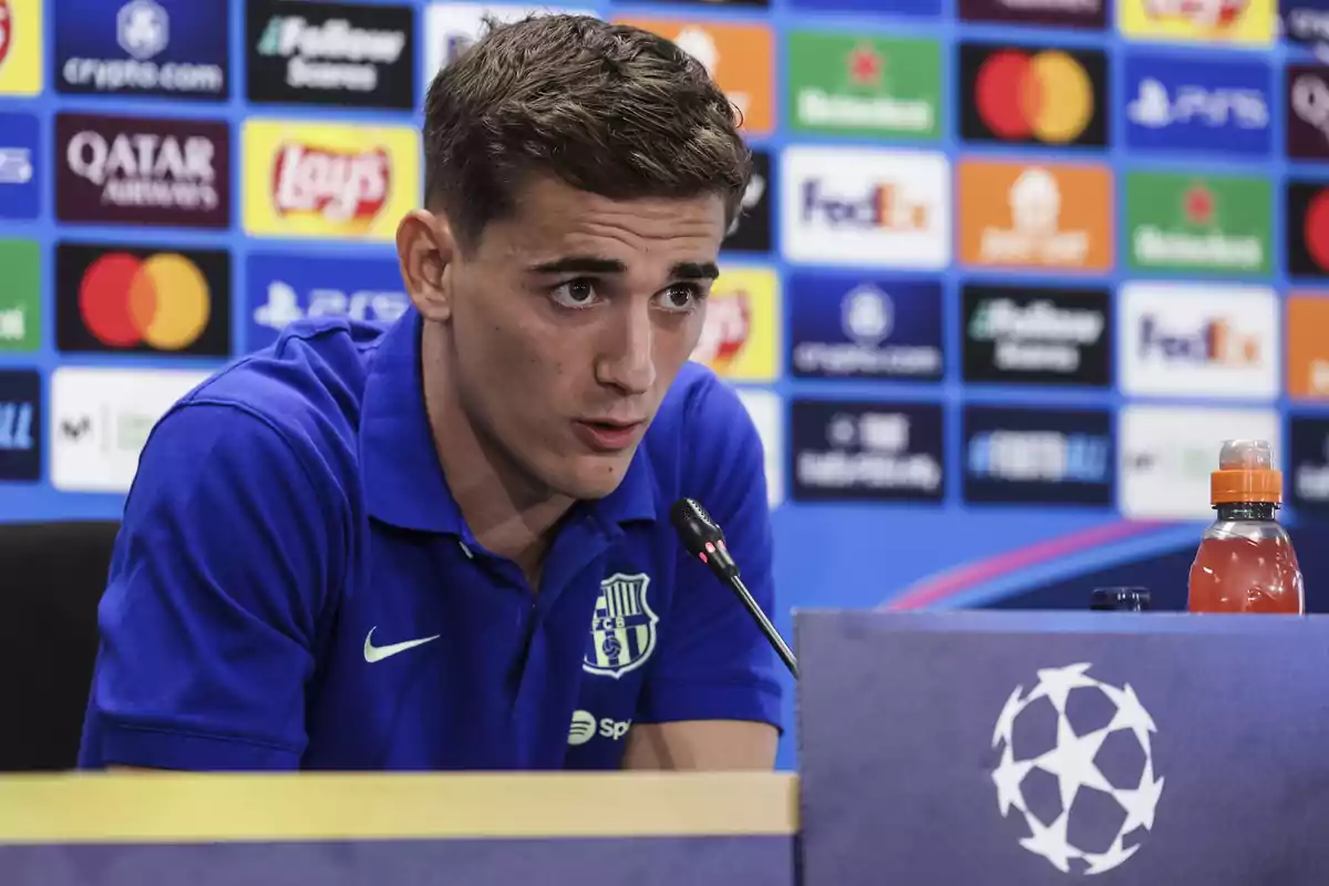 Gavi parlant en una roda de premsa de la Lliga de Campions amb un fons de patrocinadors i una ampolla de beguda esportiva sobre la taula