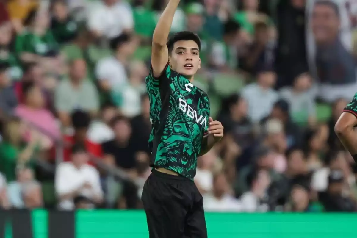 Jove futbolista amb uniforme verd i negre celebrant en un estadi ple d’aficionats