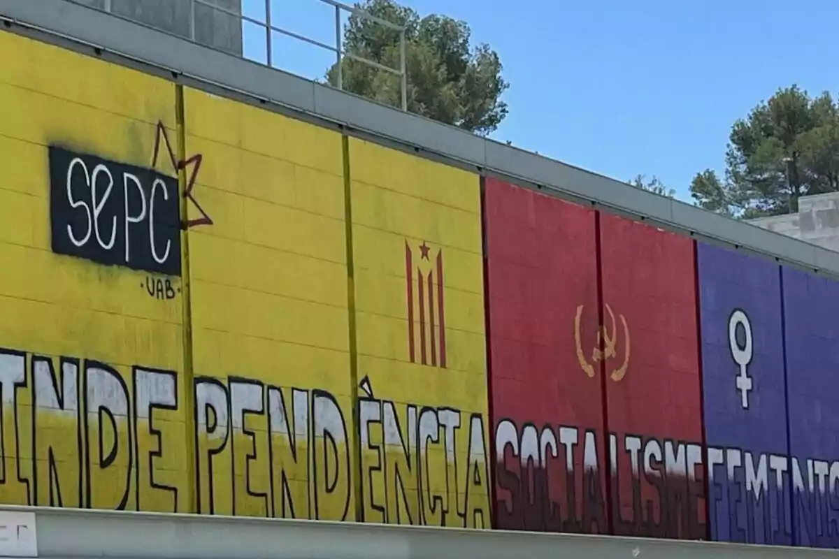 Mural pintat en una paret amb els colors groc, vermell i morat, símbols independentistes, comunistes i feministes, i les paraules independència, socialisme i feminisme.