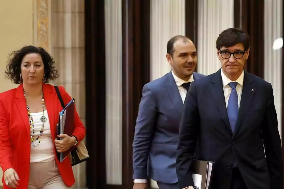 Tres personas vestidas de manera formal caminan por un pasillo con carpetas y documentos en la mano