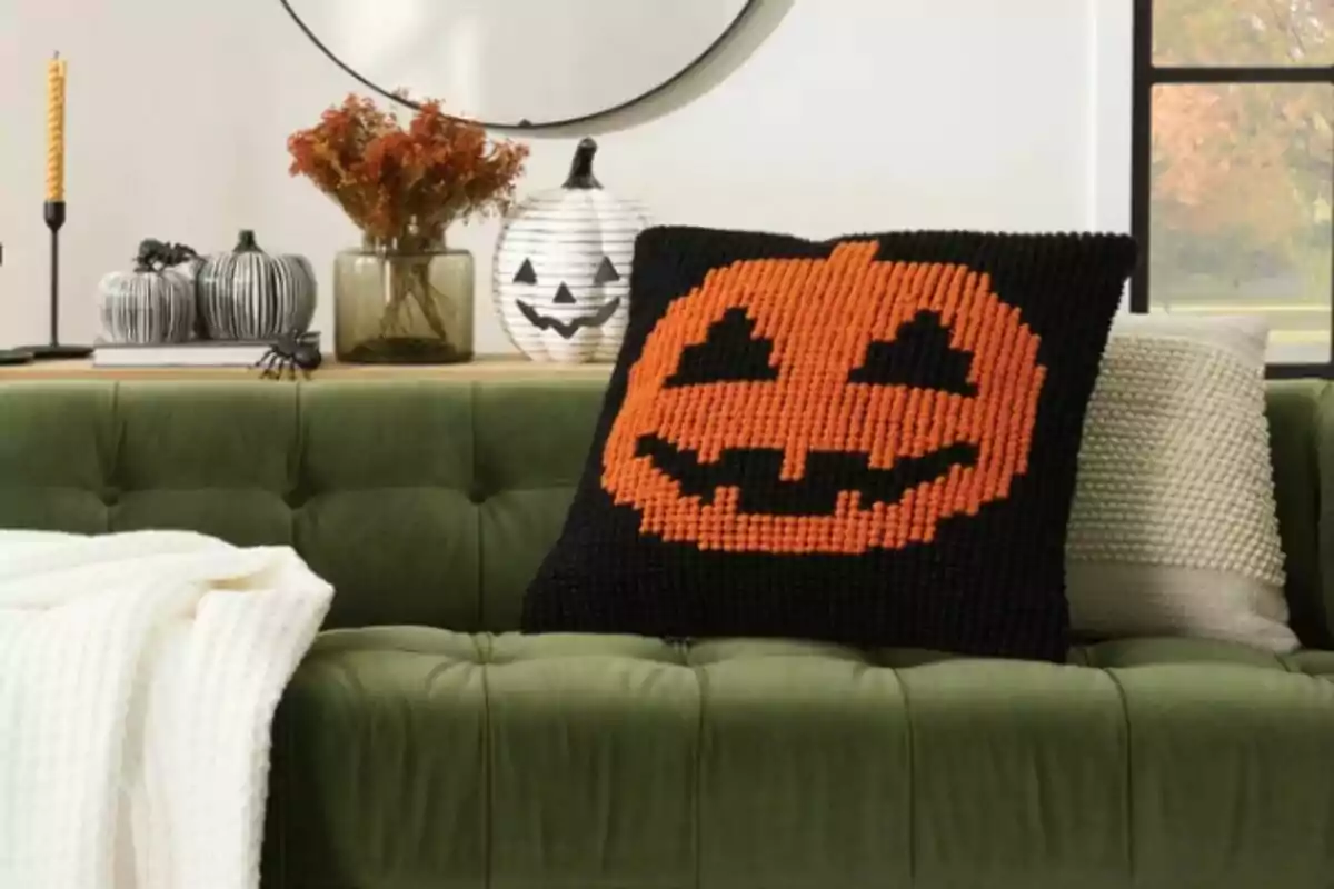 Black cushion with an orange Halloween pumpkin from Costco on a green sofa in a living room decorated for fall.