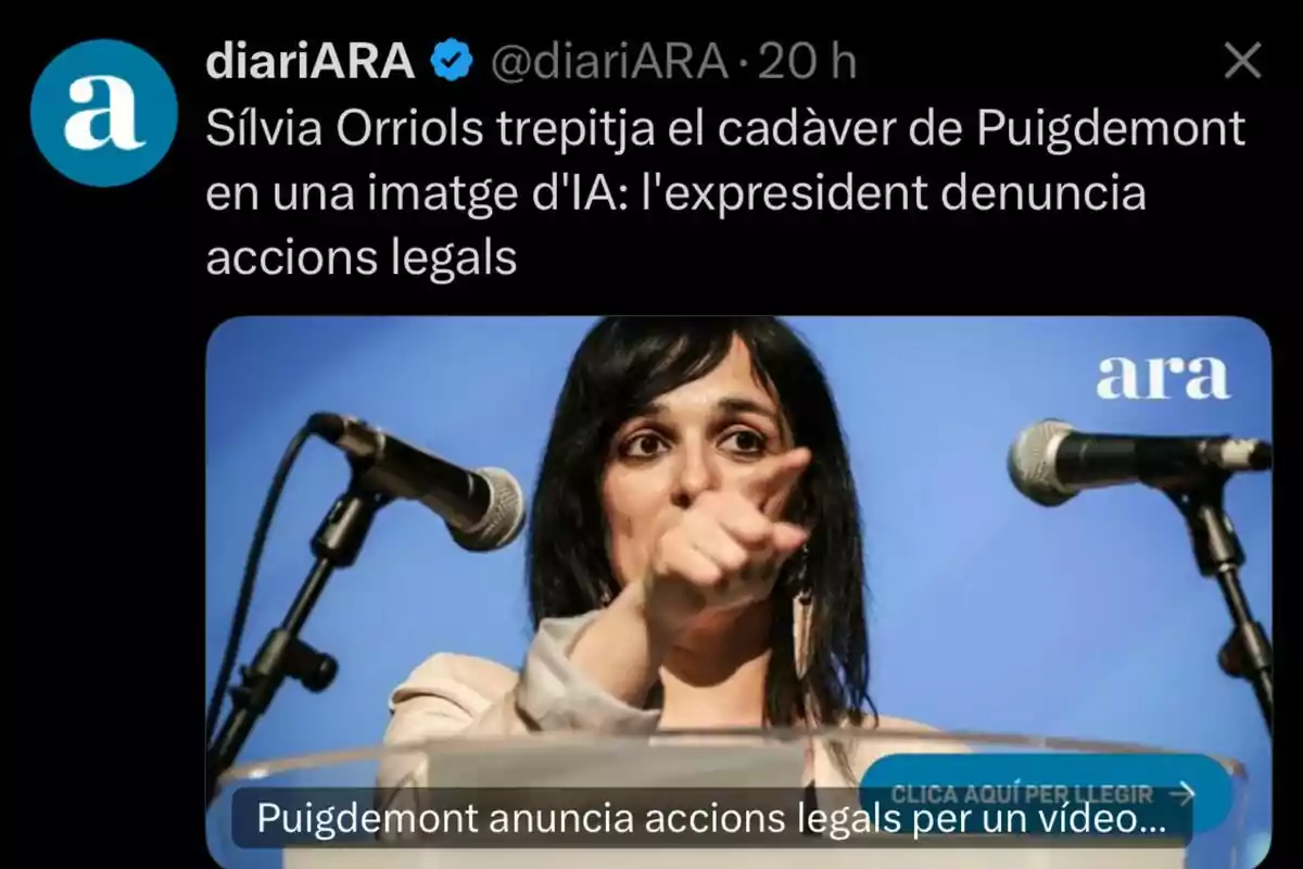 Una dona de cabell fosc assenyala amb el dit mentre parla davant de dos micròfons amb un fons blau i el logotip d’ara a la cantonada.