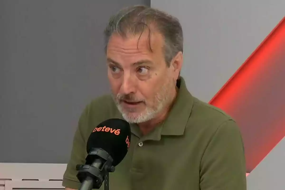 Hombre de cabello canoso y barba corta con camisa verde hablando frente a un micrófono negro en un estudio de radio