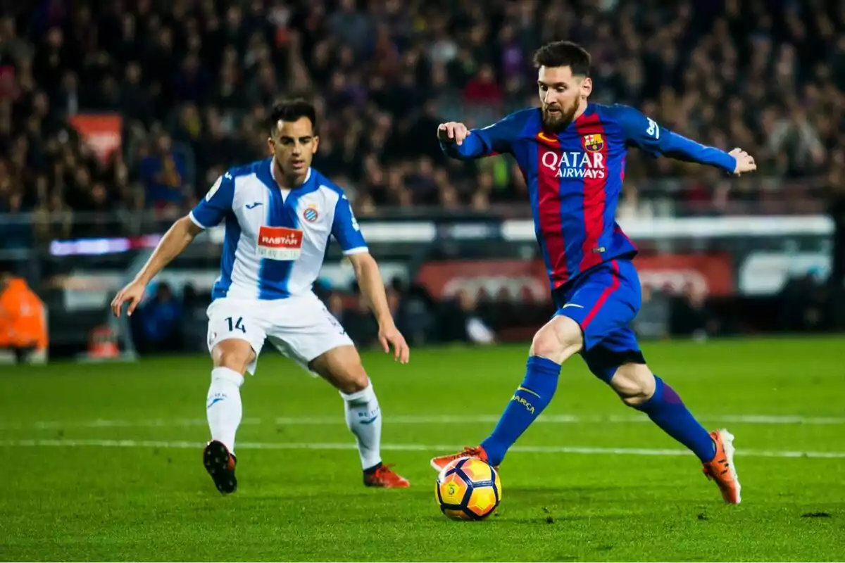 Dos futbolistes disputen la pilota durant un partit entre el Barcelona i l’Espanyol en un estadi ple d’espectadors.