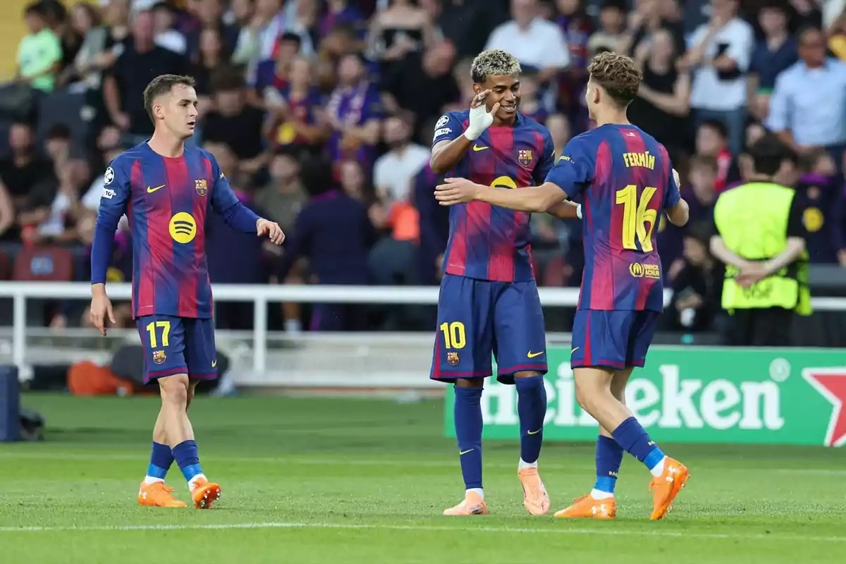 Tres jugadores del FC Barcelona celebran un gol en el campo durante un partido con aficionados en las gradas al fondo