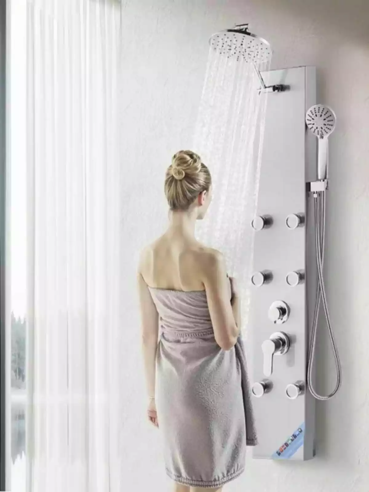 Dona d’esquena embolicada amb una tovallola davant d’una dutxa moderna amb múltiples controls en un bany il·luminat per llum natural