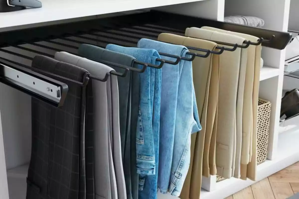 Pantalons penjats ordenadament en un organitzador metàl·lic dins d’un armari blanc