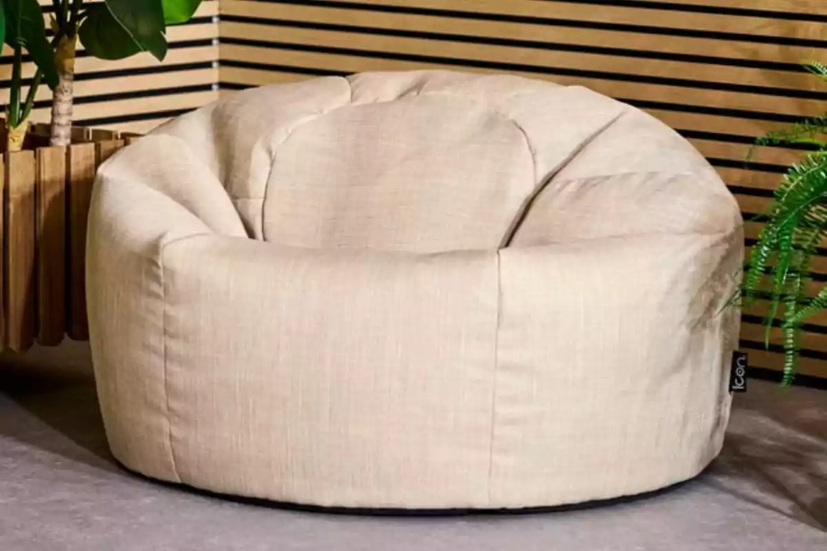 Butaca tipus puff de tela beix en una habitació amb plantes i paret de llistons de fusta Butaca tipus puff de tela beix en una habitació amb plantes i paret de llistons de fusta