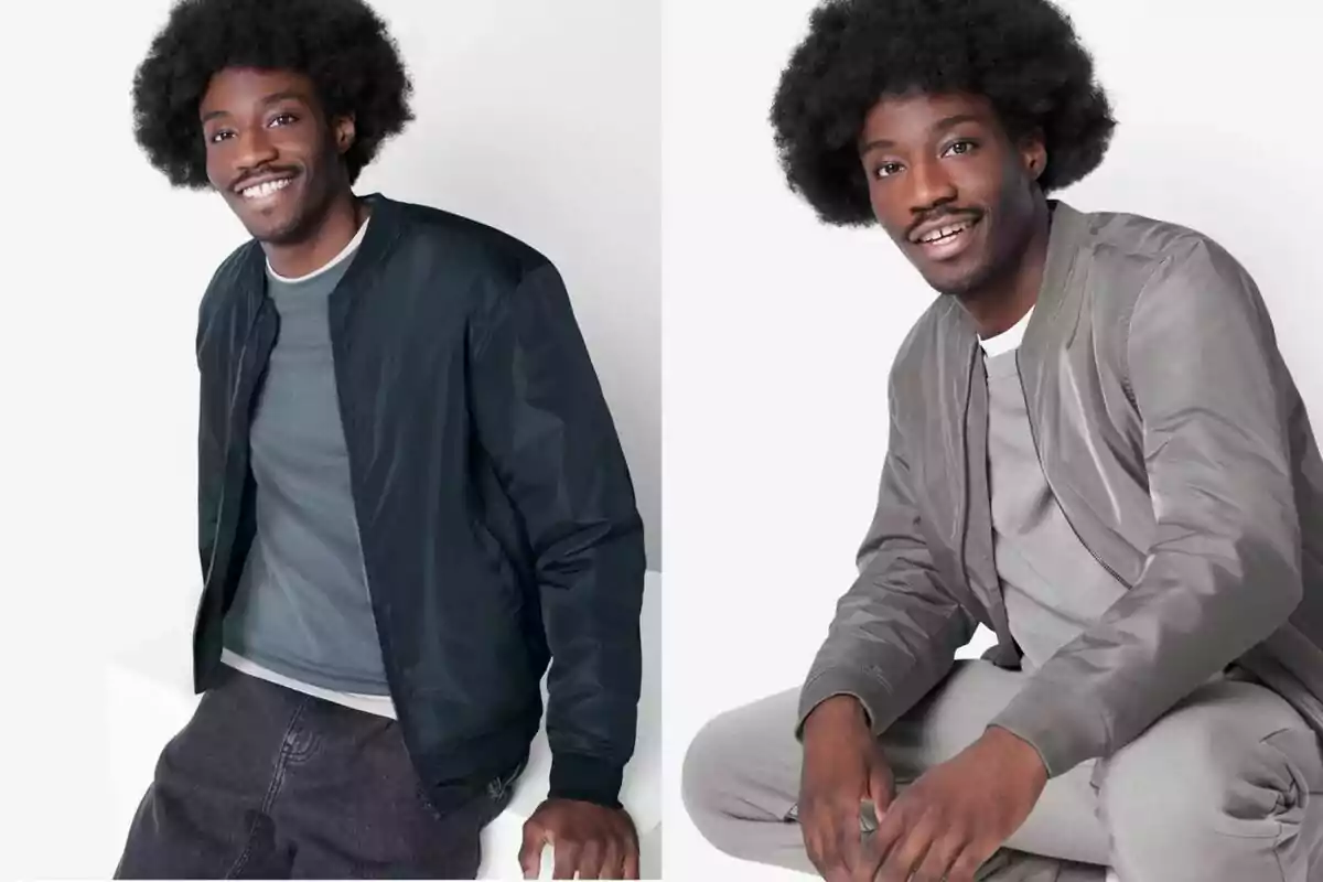 Hombre joven con cabello afro sonriente, usando chaqueta bomber en dos colores diferentes, una negra y otra gris, posando en un fondo claro