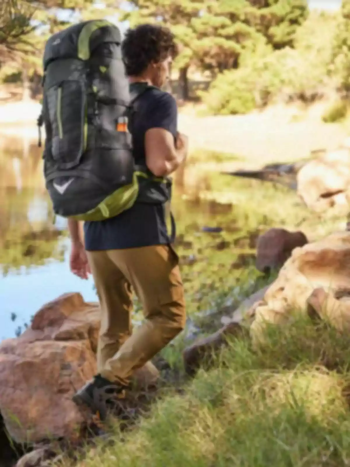 Persona con mochila grande caminando junto a un lago rodeado de naturaleza