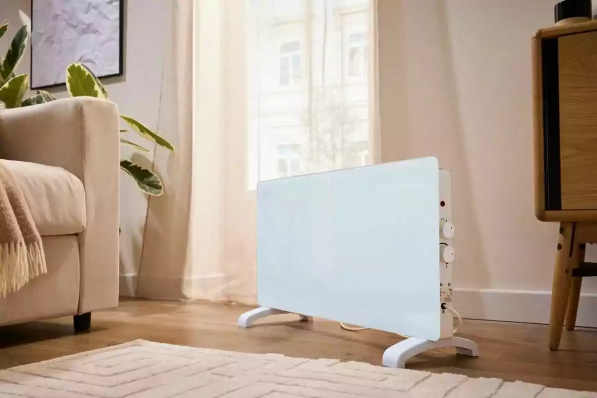 Calefactor blanc de panell col·locat en una sala al costat d’un sofà beix i una catifa clara amb llum natural entrant per la finestra