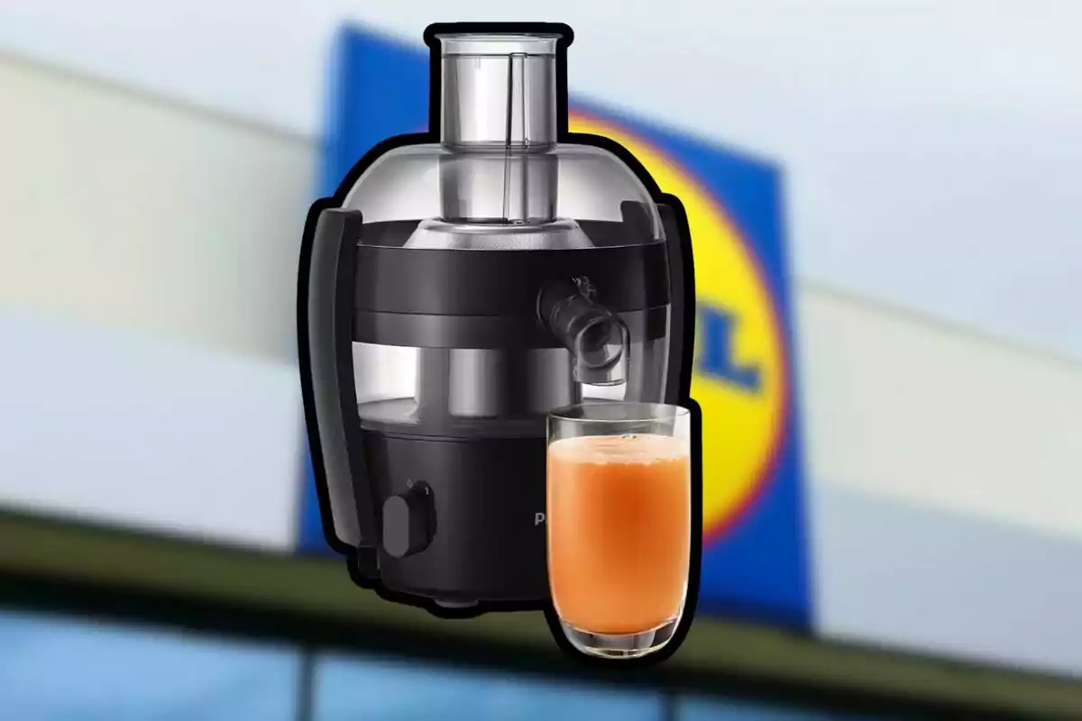 Extractor de jugos negro con un vaso de jugo naranja al frente y un fondo desenfocado de una tienda con logotipo azul y amarillo