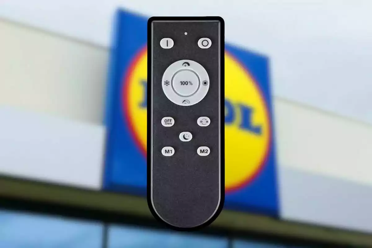 Control remoto negro con varios botones frente a un cartel borroso de una tienda Lidl