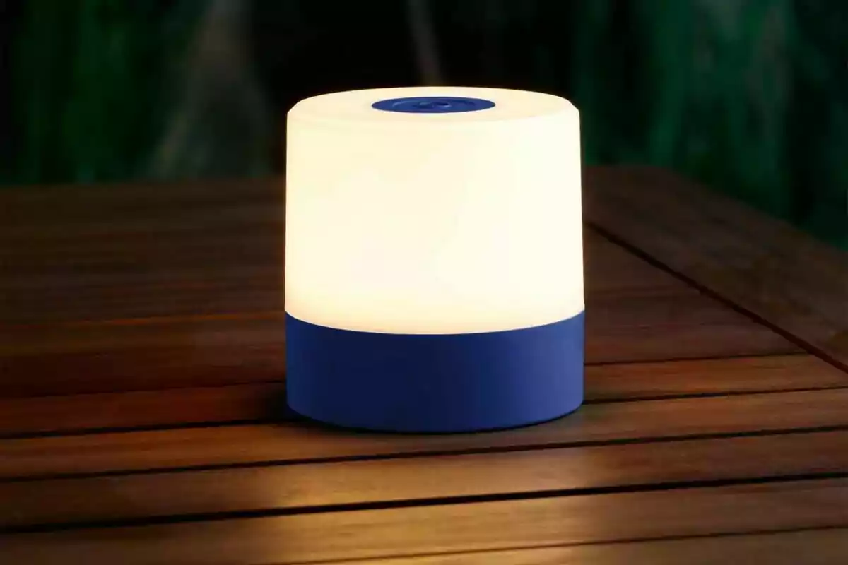Làmpada portàtil de llum càlida amb base blava sobre una taula de fusta