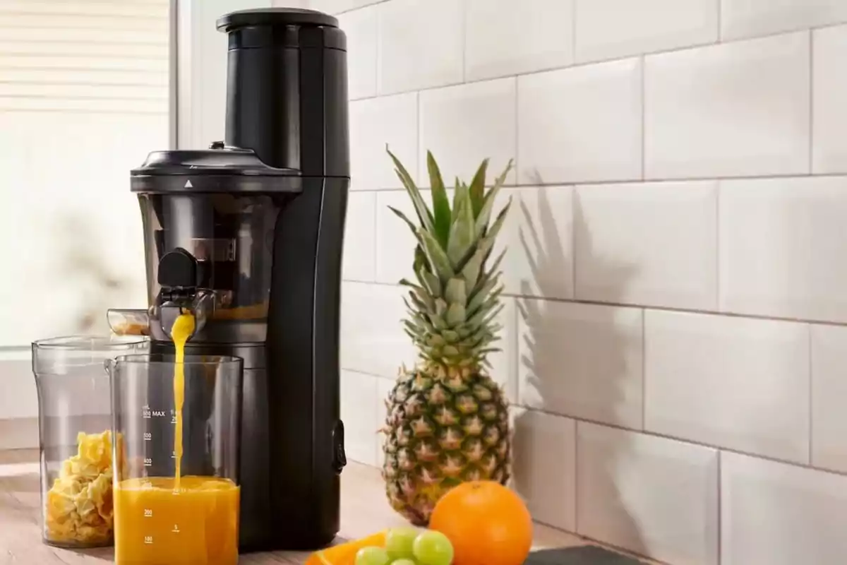 Extractor de jugos eléctrico en una cocina con piña, naranja y uvas sobre la mesa
