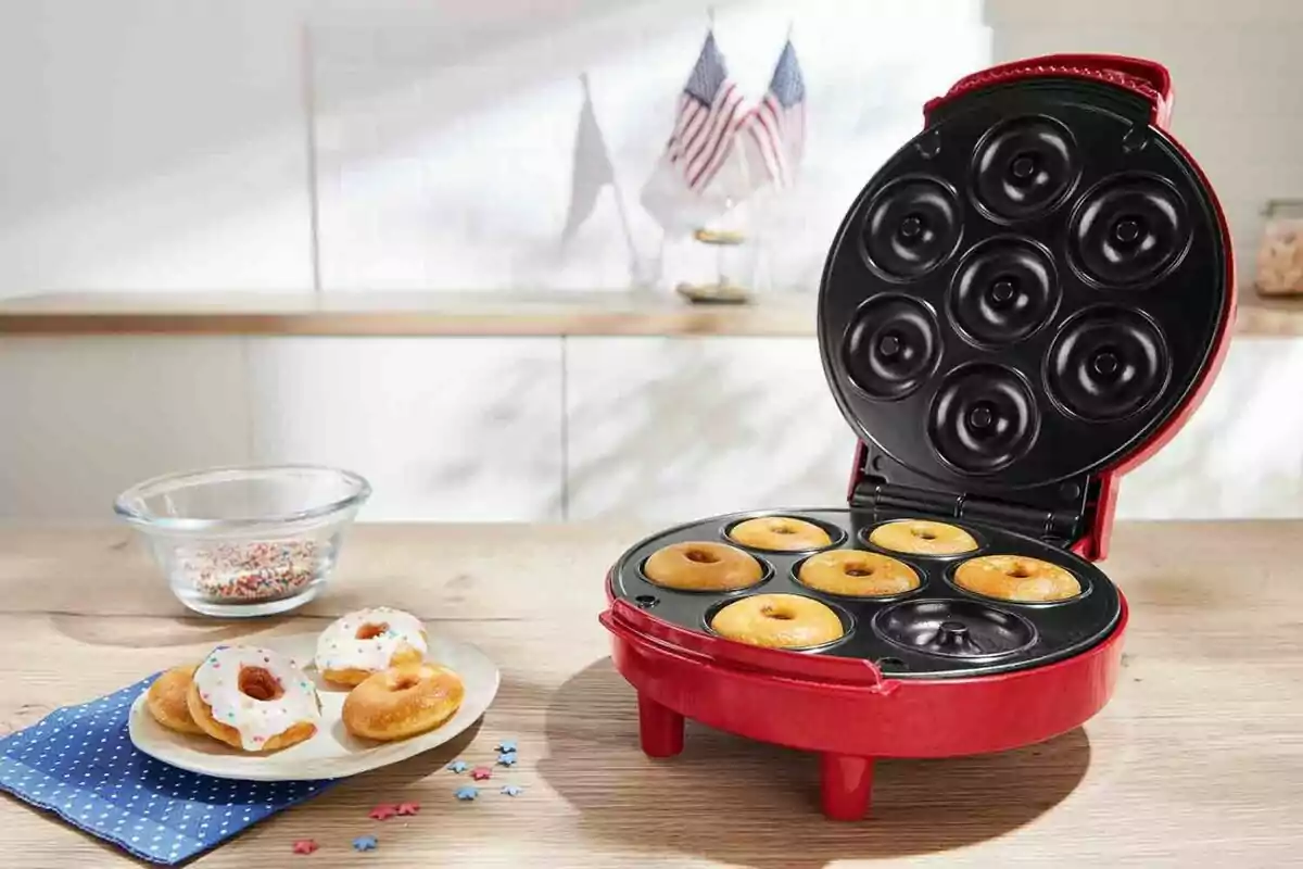 Màquina vermella per fer bunyols petits amb diversos bunyols acabats de fer i un plat amb bunyols decorats al davant sobre una taula de fusta.