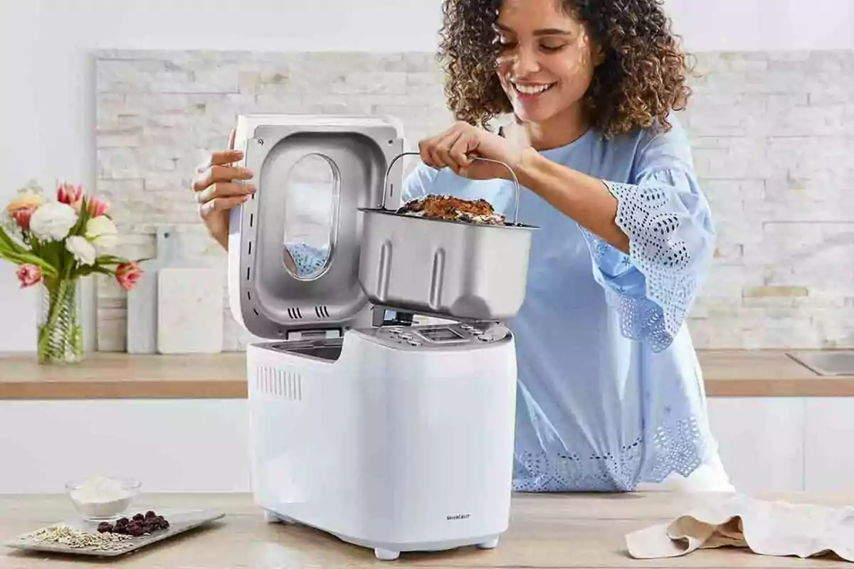 Dona somrient traient el recipient d'una panificadora elèctrica en una cuina moderna