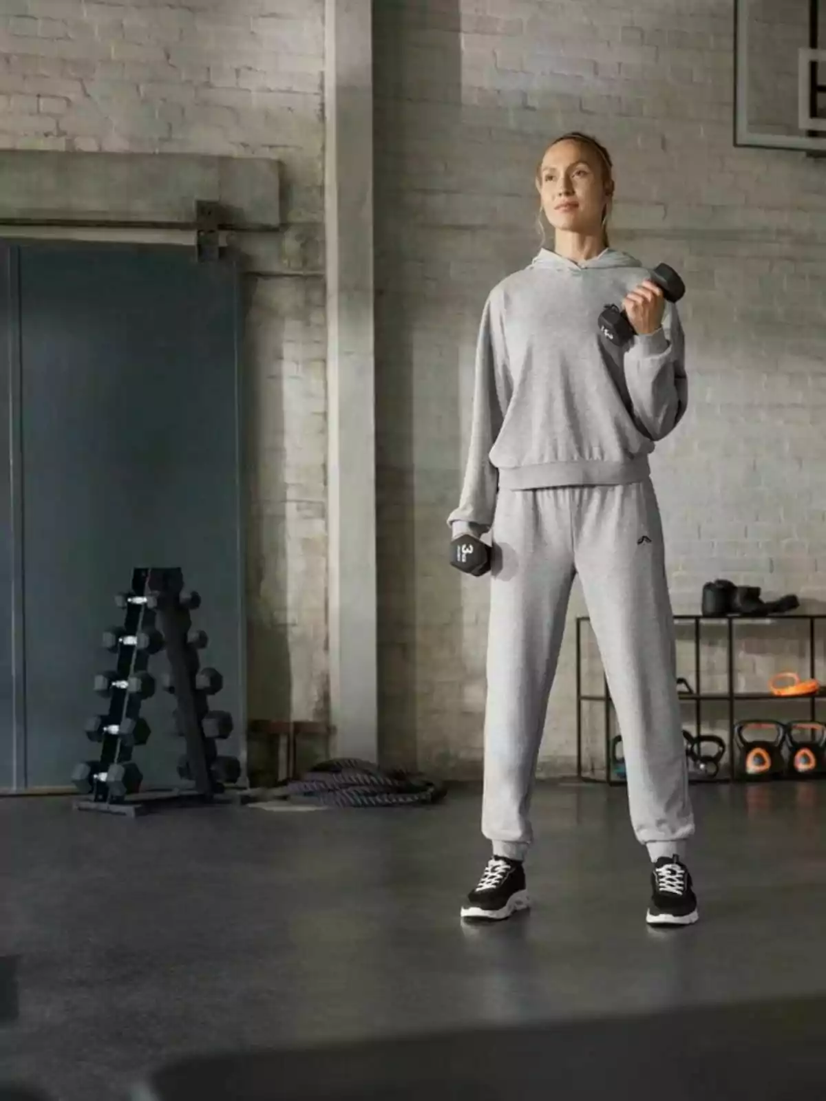 Mujer con ropa deportiva gris levantando pesas en un gimnasio industrial