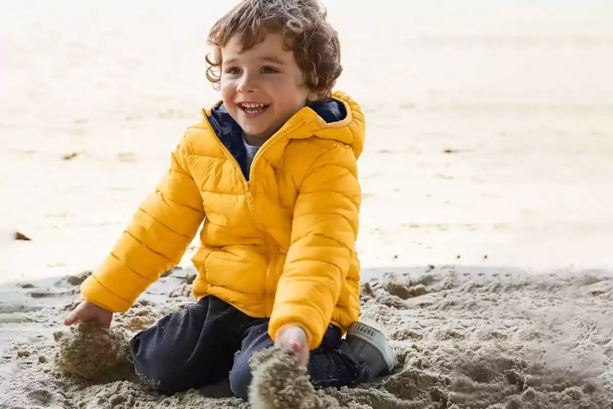 Nen petit amb jaqueta groga jugant i somrient a la sorra
